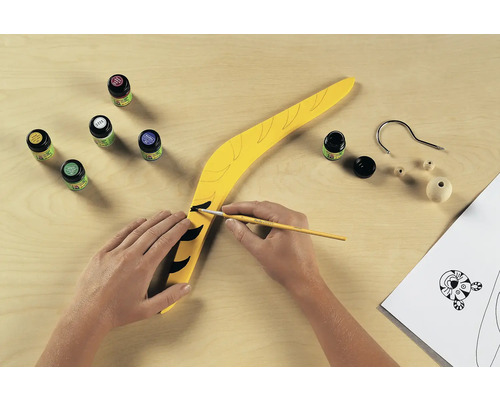 Gele boemerang wordt beschilderd met verf en penseel, knutselmateriaal ligt klaar.