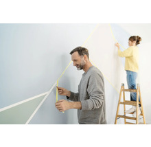 Twee mensen decoreren een muur met schilderstape en geometrische vormen.
