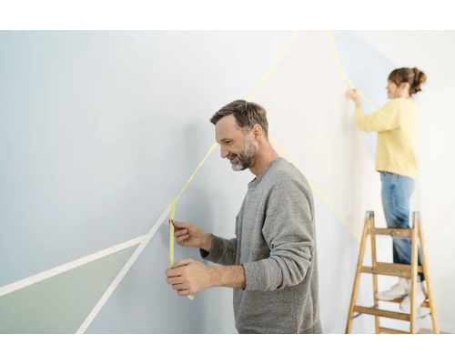 Twee mensen decoreren een muur met schilderstape en geometrische vormen.