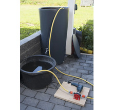 Regenwatertank met kraan, emmer met water, boormachine en pomp op stenen vloer