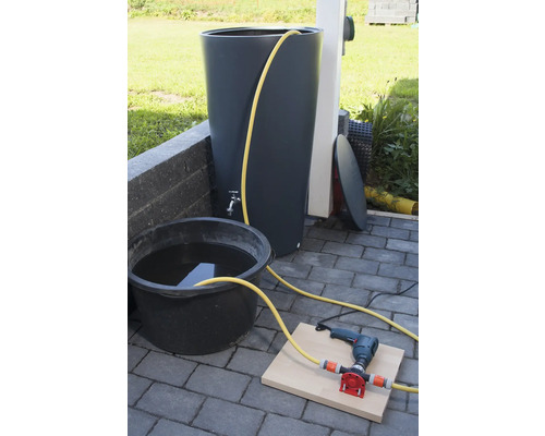 Regenwatertank met kraan, emmer met water, boormachine en pomp op stenen vloer