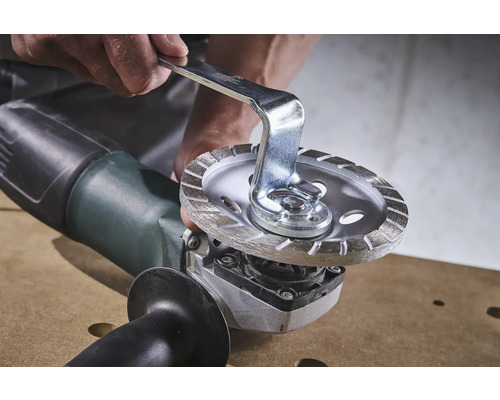 Persoon verwisselt een doorslijpschijf op een haakse slijper met een steeksleutel.