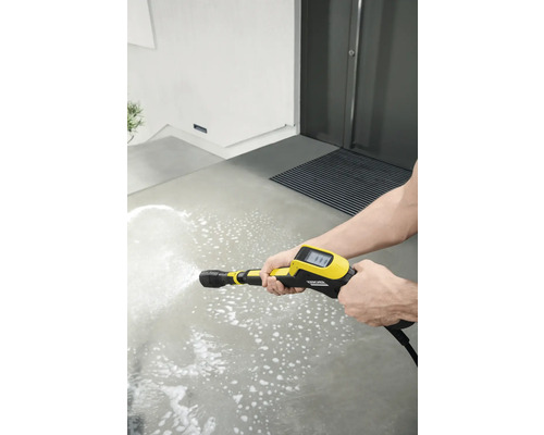 Een persoon reinigt een betonnen oppervlak met een gele hogedrukreiniger.