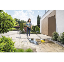 Vrouw reinigt bestrating met een terrasreiniger van Kärcher voor een huis.