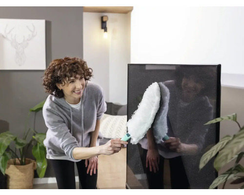 Vrouw maakt een flatscreen-tv schoon met een plumeau in een heldere woonkamer.