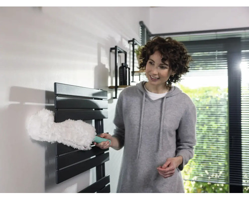 Vrouw maakt radiator schoon met een plumeau