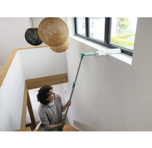 Vrouw maakt raamkozijn schoon met plumeau op telescopische steel in trappenhuis