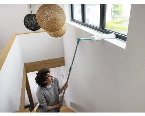 Vrouw maakt raamkozijn schoon met plumeau op telescopische steel in trappenhuis