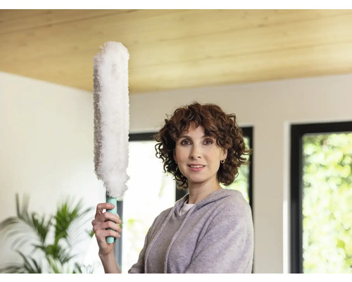 Vrouw houdt stofdoek vast in een lichte kamer.
