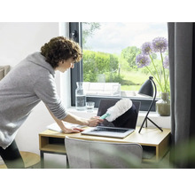 Vrouw maakt laptop schoon met een plumeau op een bureau.