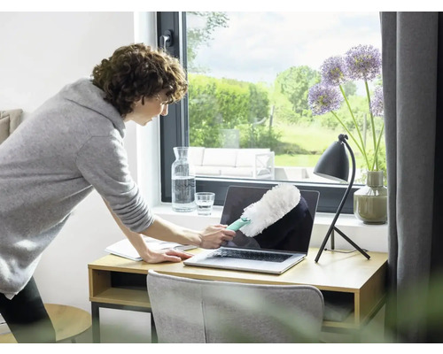 Vrouw maakt laptop schoon met een plumeau op een bureau.