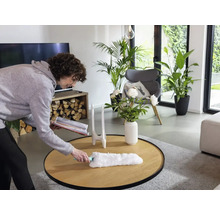 Vrouw stoffert een tafel in een lichte woonkamer met een plumeau.