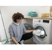 Vrouw legt dweilhoezen in de wasmachine in een lichte kamer.