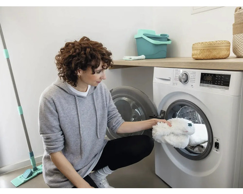 Vrouw legt dweilhoezen in de wasmachine in een lichte kamer.