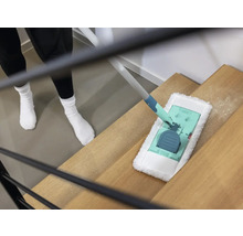 Een persoon maakt een houten trap schoon met een vloermop.