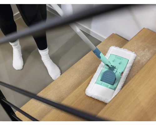 Een persoon maakt een houten trap schoon met een vloermop.