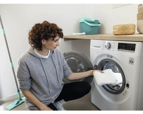 Vrouw stopt een wasbare vloermopdoek in een wasmachine.