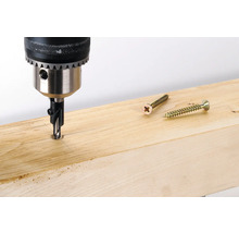 Boormachine met verzinkboor boort in een houten plank, daarnaast liggen twee schroeven