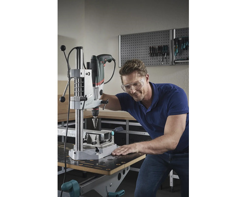 Man met veiligheidsbril boort met een kolomboormachine in een werkplaats