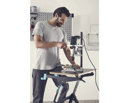 Man met veiligheidsbril boort met een boormachine in een werkstuk op een werkbank.