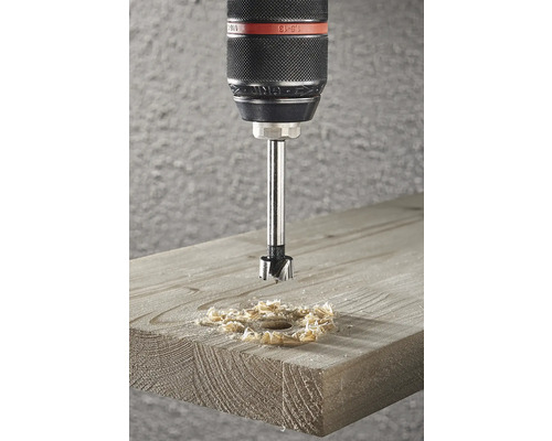 Forstnerboor bezig met het boren van een gat in een houten plank, waarbij houtsnippers ontstaan.