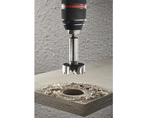 Forstnerboor op een boormachine boven een houten plank met een geboord gat