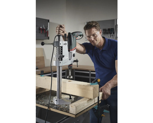 Een man boort met een tafelboormachine een gat in een houten plank.