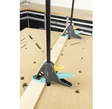 Twee éénhandsklemmen fixeren een houten plank op een werkbank.