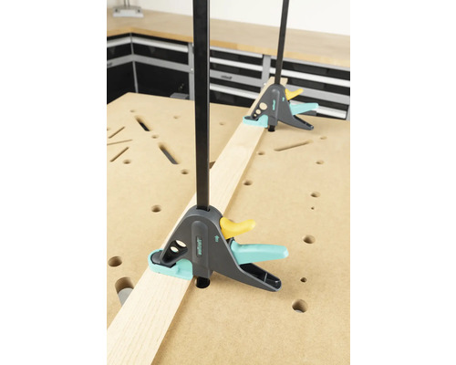 Twee éénhandsklemmen fixeren een houten plank op een werkbank.