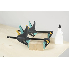 Twee Wolfcraft eenhandsklemmen fixeren houten stukken op een werkbank, een fles lijm staat ernaast.