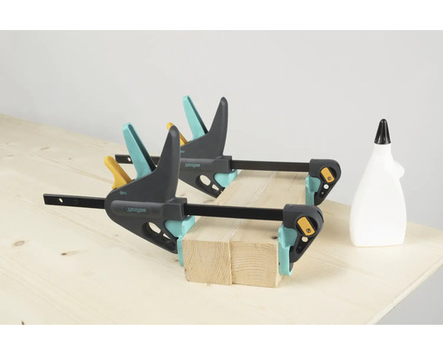 Twee Wolfcraft eenhandsklemmen fixeren houten stukken op een werkbank, een fles lijm staat ernaast.