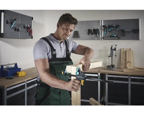 Man fixeert houten stukken met een eenhandsklem in een werkplaats.