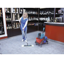 Schoonmaakster dweilt een tegelvloer in een wijnwinkel met een mop en emmer.