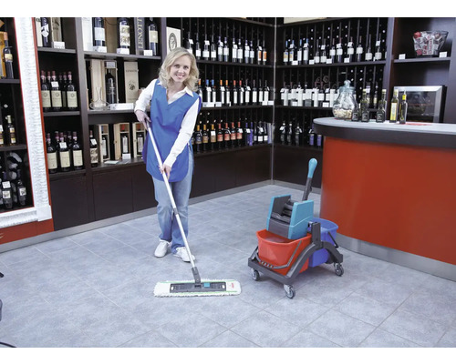 Schoonmaakster dweilt een tegelvloer in een wijnwinkel met een mop en emmer.