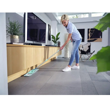 Vrouw dweilt de vloer in de woonkamer met een mop.