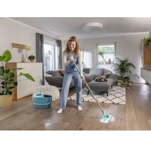 Vrouw dweilt houten vloer met een mop en een emmer in een woonkamer