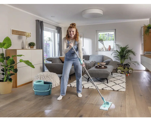 Vrouw dweilt houten vloer met een mop en een emmer in een woonkamer