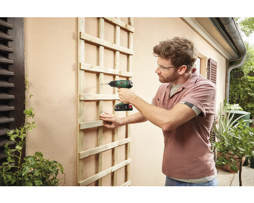 Man bevestigt houten trellis met accuschroevendraaier aan de muur van het huis