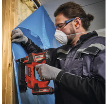 Man bevestigt een folie aan een houten constructie met een accutacker. Hij draagt een veiligheidsmasker en een veiligheidsbril.