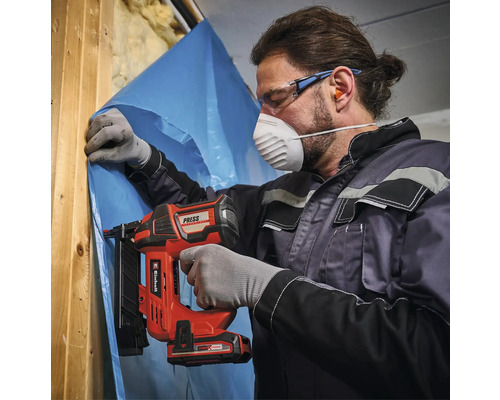 Man bevestigt een folie aan een houten constructie met een accutacker. Hij draagt een veiligheidsmasker en een veiligheidsbril.