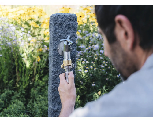 Tuinscène met kraan op stenen zuil en een persoon die een slang aansluit
