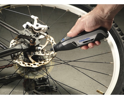 Dremel Logo. Een persoon gebruikt een Dremel Lite gereedschap op een fietsremschijf.