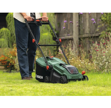 Een persoon bedient een groene Bosch grasmaaier op een gazon.