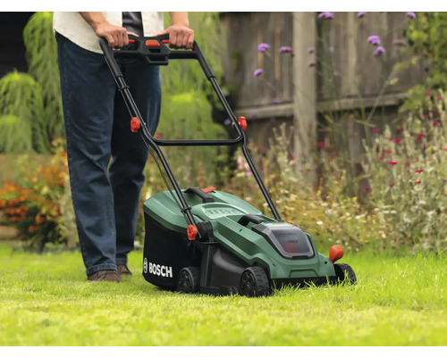 Een persoon bedient een groene Bosch grasmaaier op een gazon.