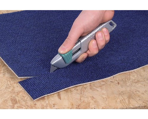 Een hand snijdt met een tapijtmes een tapijt.