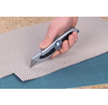 Een hand snijdt karton met een stanleymes.