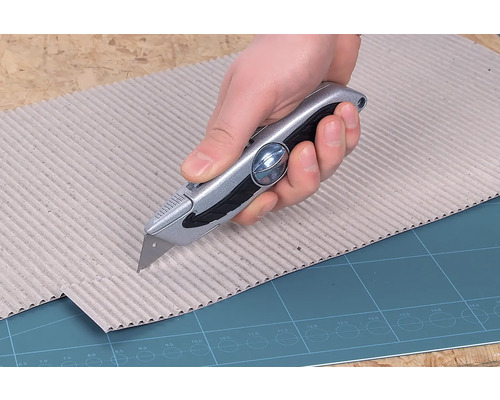 Een hand snijdt karton met een stanleymes.