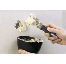 Een gat in een muur wordt gerepareerd met een plamuurmes en vulmiddel.