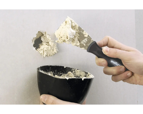 Een gat in een muur wordt gerepareerd met een plamuurmes en vulmiddel.