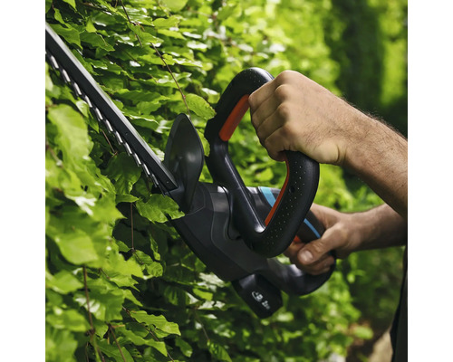 Persoon gebruikt een heggenschaar om een haag te knippen